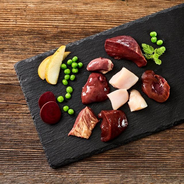 Selection of fresh organ meats and complementary pet-food ingredients on a slate board